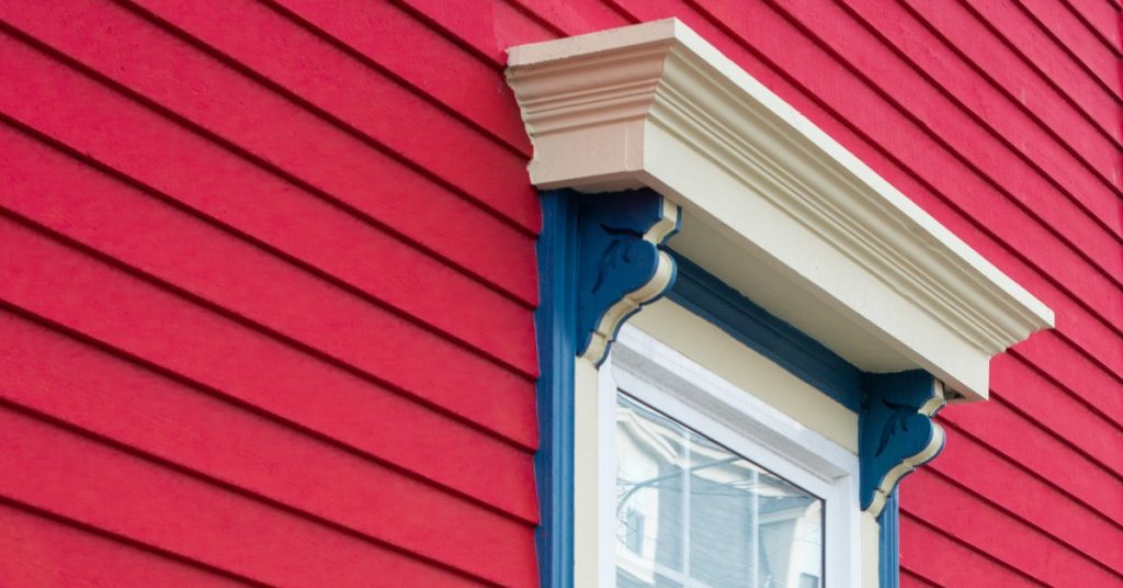 A red residential home with a custom, decorative window. The window features a decorative moulding above the millwork.