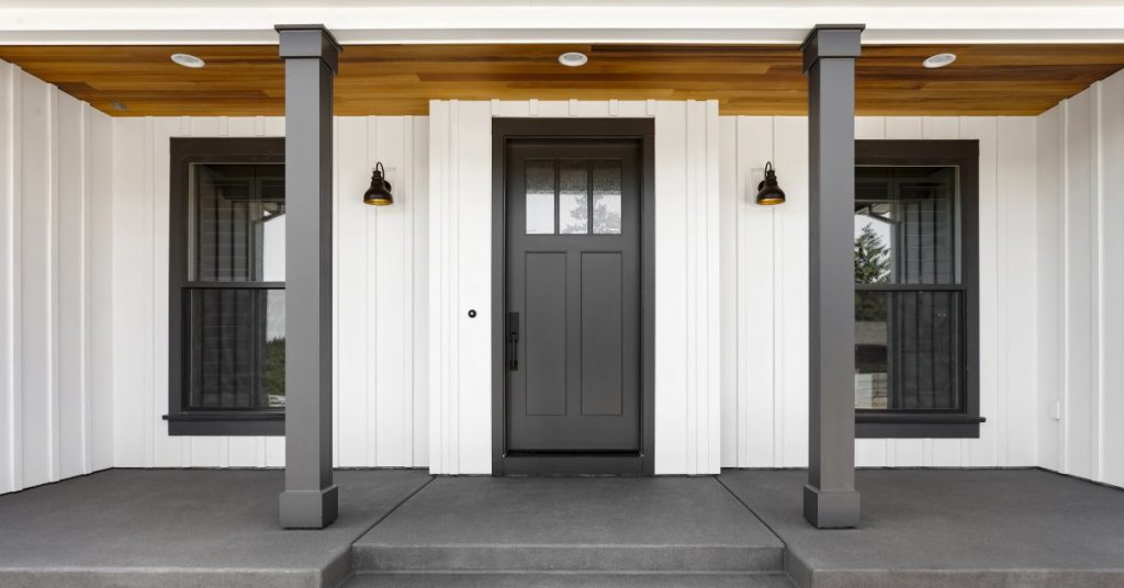 A farmhouse front entrance featuring black doors and window frames and columns with aluminum wraps that simulate wood.