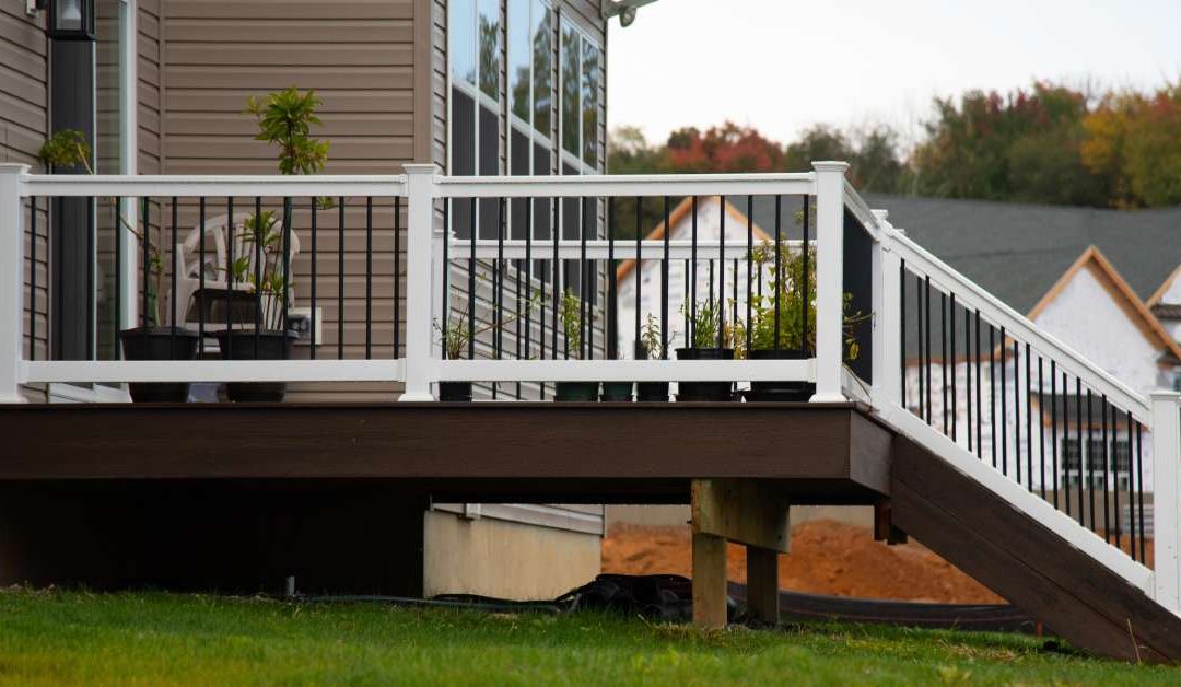 The backside of a home with taupe siding, a sliding door, and stairs of a dark brown deck with white railings.